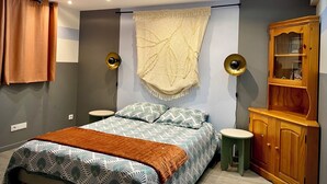 Une chambre à coucher comprenant un lit, deux tables de chevet, une armoire en bois et un luminaire fixé au plafond.