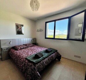 Un dormitorio con cama, una ventana, una obra de arte colgada en la pared y una lámpara en el techo.