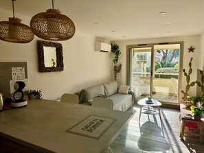 Une cuisine moderne dotée d’un îlot central, d’un coin repas avec une table et des chaises, et d’une porte-fenêtre coulissante donnant sur un balcon agrémenté de plantes et offrant une vue sur l’extérieur.