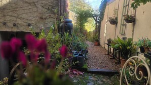 Un jardin avec des plantes en pot, un mur de pierre et une chaise en métal.