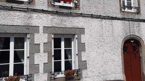 Un immeuble avec trois fenêtres, chacune dotée d’un balcon et de jardinières. On y trouve une porte rouge sur laquelle est inscrit le numéro « 22 ».