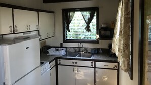Eine kleine Küche mit weißen Schränken, einer Spüle und einem Fenster mit Vorhängen.