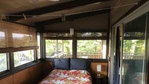 Ein Schlafzimmer mit Bett, Nachttisch, Fenster mit Jalousien und Blick auf Grünfläche.