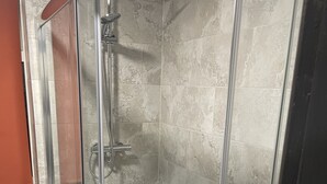 Una ducha con cerramiento de vidrio, cabezal de ducha de mano y grifo empotrado.