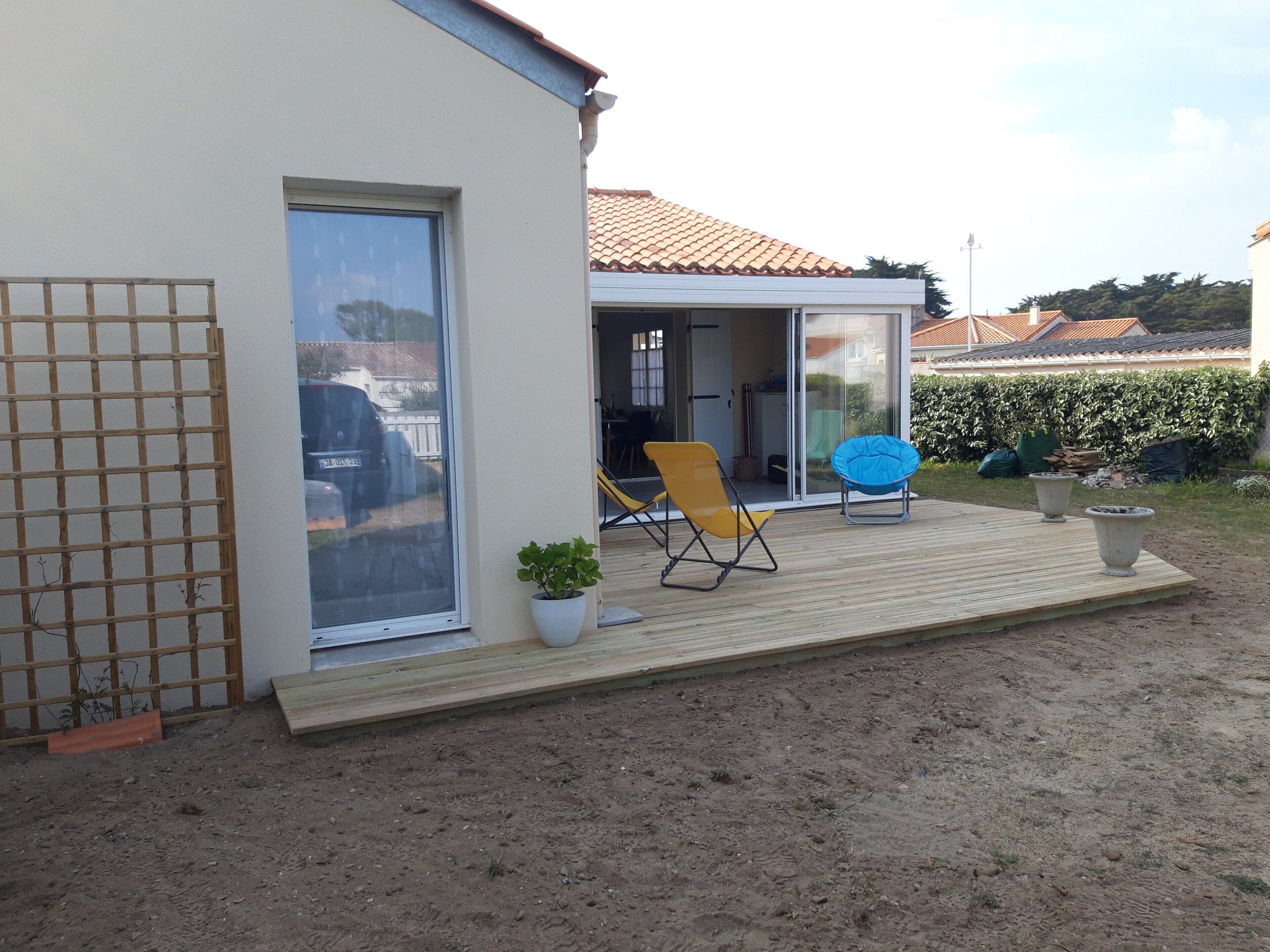 A house with a patio, a sliding glass door, a wooden deck, and two chairs.
