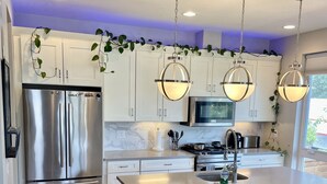 A modern kitchen with a stainless steel refrigerator, a central island with bar stools, and pendant lighting. - Rooftop + pool table + hot tub near Broncos Stadium! (Denver)