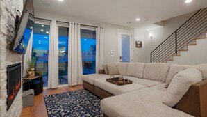 A modern living room with a sectional sofa, a fireplace, a TV mounted on the wall, and a staircase. - Rooftop + pool table + hot tub near Broncos Stadium! (Denver)