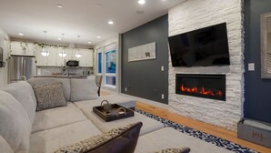 A modern living room with a sofa, a fireplace, and a kitchen in the background. - Rooftop + pool table + hot tub near Broncos Stadium! (Denver)
