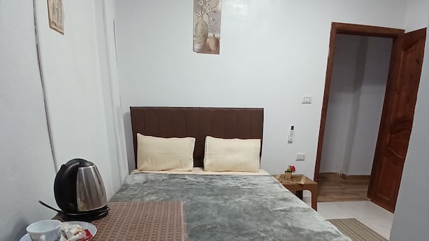 A hotel room with a bed, bedside table, and a small table with a cup and saucer. - Pyramids home stay view (Giza)
