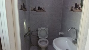 A small bathroom with a toilet, sink, and shelves with toiletries. - Pyramids home stay view (Giza)