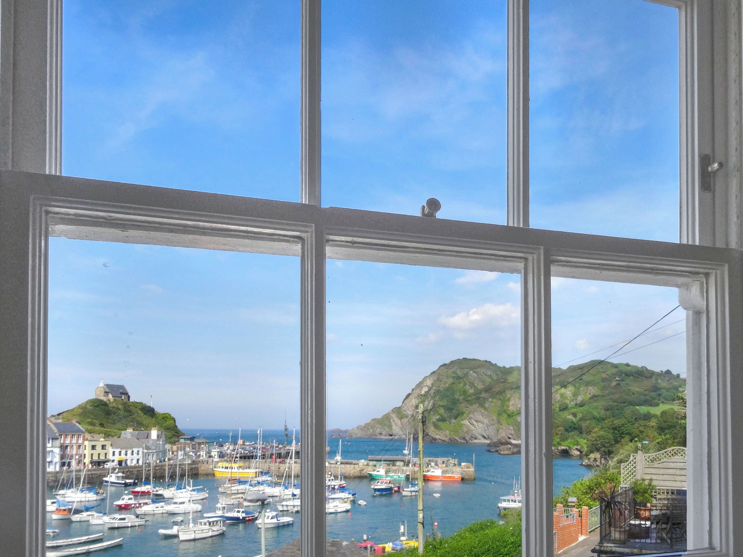 Un port avec des bateaux, une colline surmontée d’un bâtiment et un ciel dégagé.