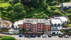 An aerial view of a town with a prominent red brick building, a white building with a grey roof, and a parking area with cars. - 1 bedroom accommodation in Ilfracombe (Ilfracombe)