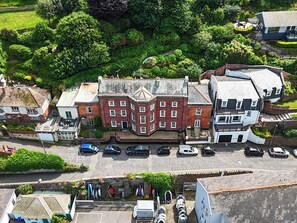 Eine Vogelperspektive einer Stadt mit einem markanten, roten Backsteinhaus, einem weißen Gebäude mit grauem Dach und einem Parkplatz mit Autos.