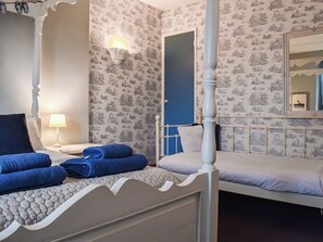 A bedroom with a four-poster bed, a nightstand with a lamp, and a blue door.