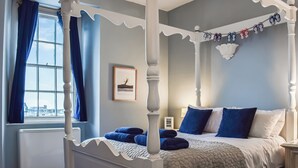 A four-poster bed with a quilted bedspread, a framed picture on the wall, and a window with curtains. - 1 bedroom accommodation in Ilfracombe (Ilfracombe)