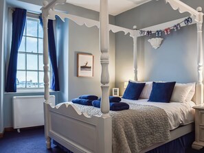 Ein Bett mit Baldachin, eine gesteppte Tagesdecke, ein gerahmtes Bild an der Wand und ein Fenster mit Vorhängen.