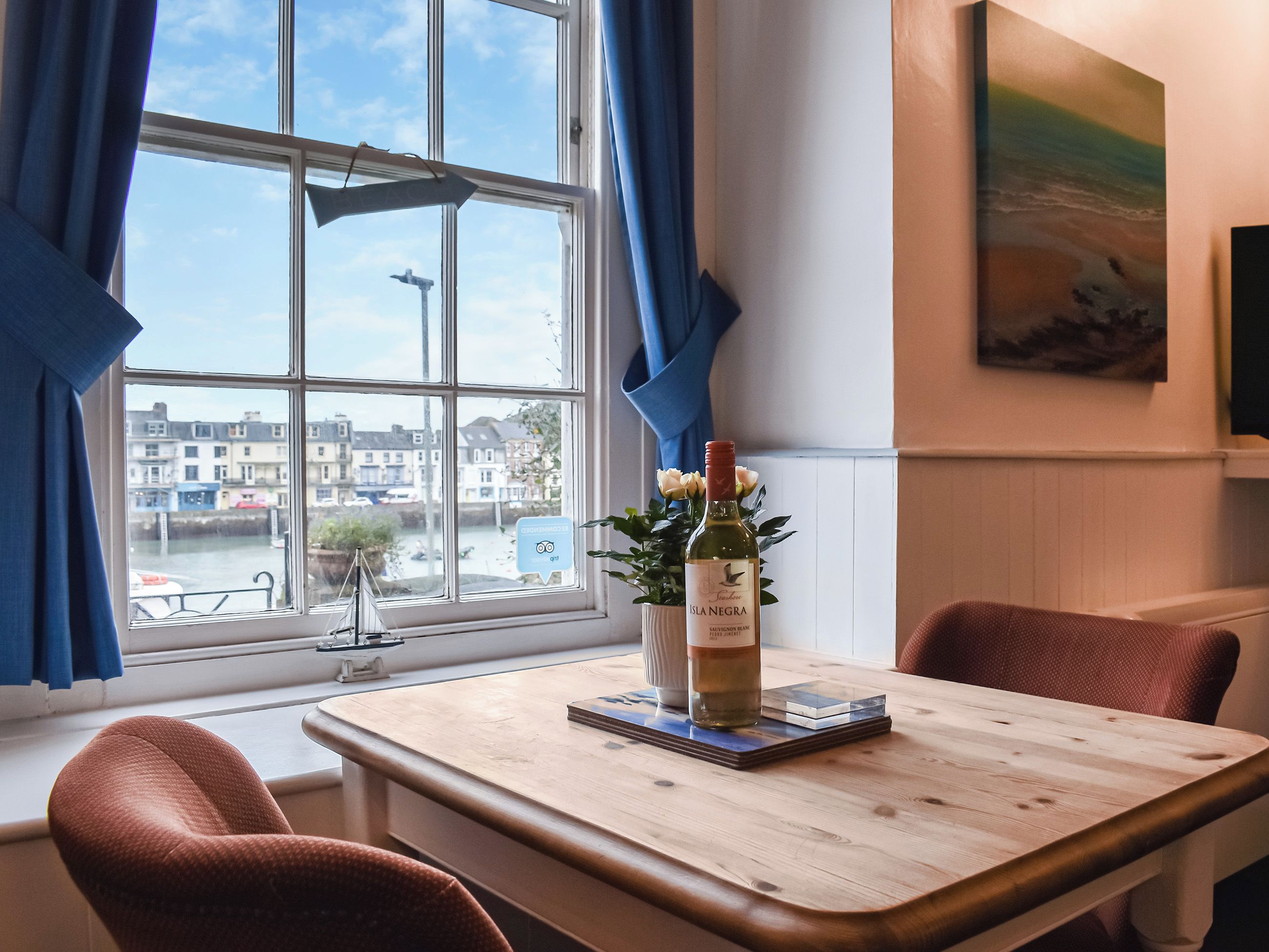 A room with a window view of a town, a table with a bottle of wine, and a chair.