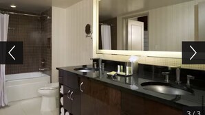 Un baño moderno con bañera, dos lavamanos, un espejo grande y un inodoro.