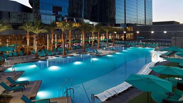Una amplia piscina cubierta con varias zonas de descanso y palmeras, rodeada de edificios altos.