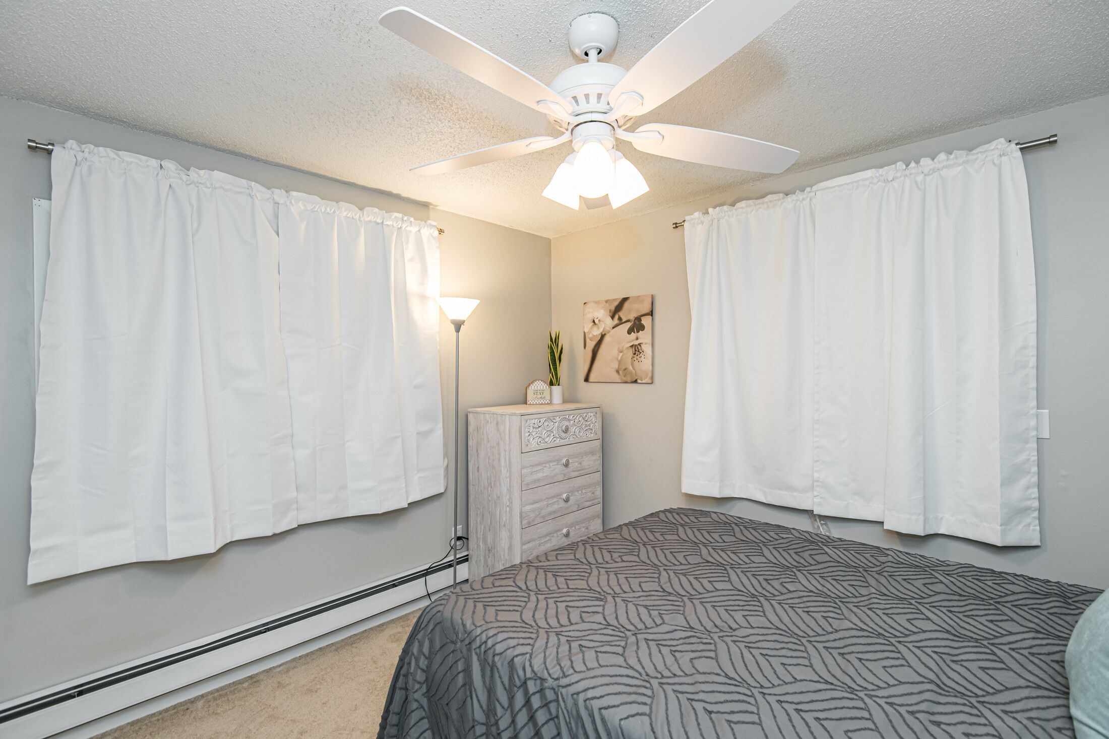 Un dormitorio con cama, ventilador de techo, cómoda y lámpara de pared.