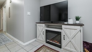 A living room with a flat-screen TV on a white entertainment center, a fireplace, and a hallway with a rug.