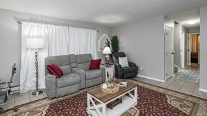 A living room with a grey sofa, a black armchair, a wooden coffee table, and a patterned rug.