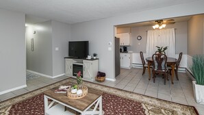 A modern living room with a TV, dining table, and kitchen area.