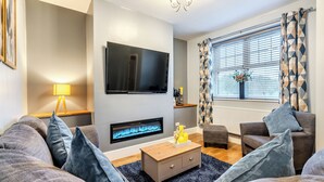 A modern living room with a flat-screen TV, a fireplace, a sofa, a coffee table, and a window with patterned curtains. - Totally refurbished cottage, decorated and equipped to a high standard. (Cornsay Colliery, Lanchester, Durham)