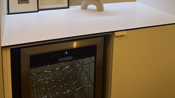 Una cocina con encimera blanca, paneles de madera en la pared, lavavajillas y un tazón decorativo con frutas.