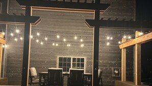 Un patio al aire libre con una pérgola de madera, luces colgantes y una mesa con sillas.
