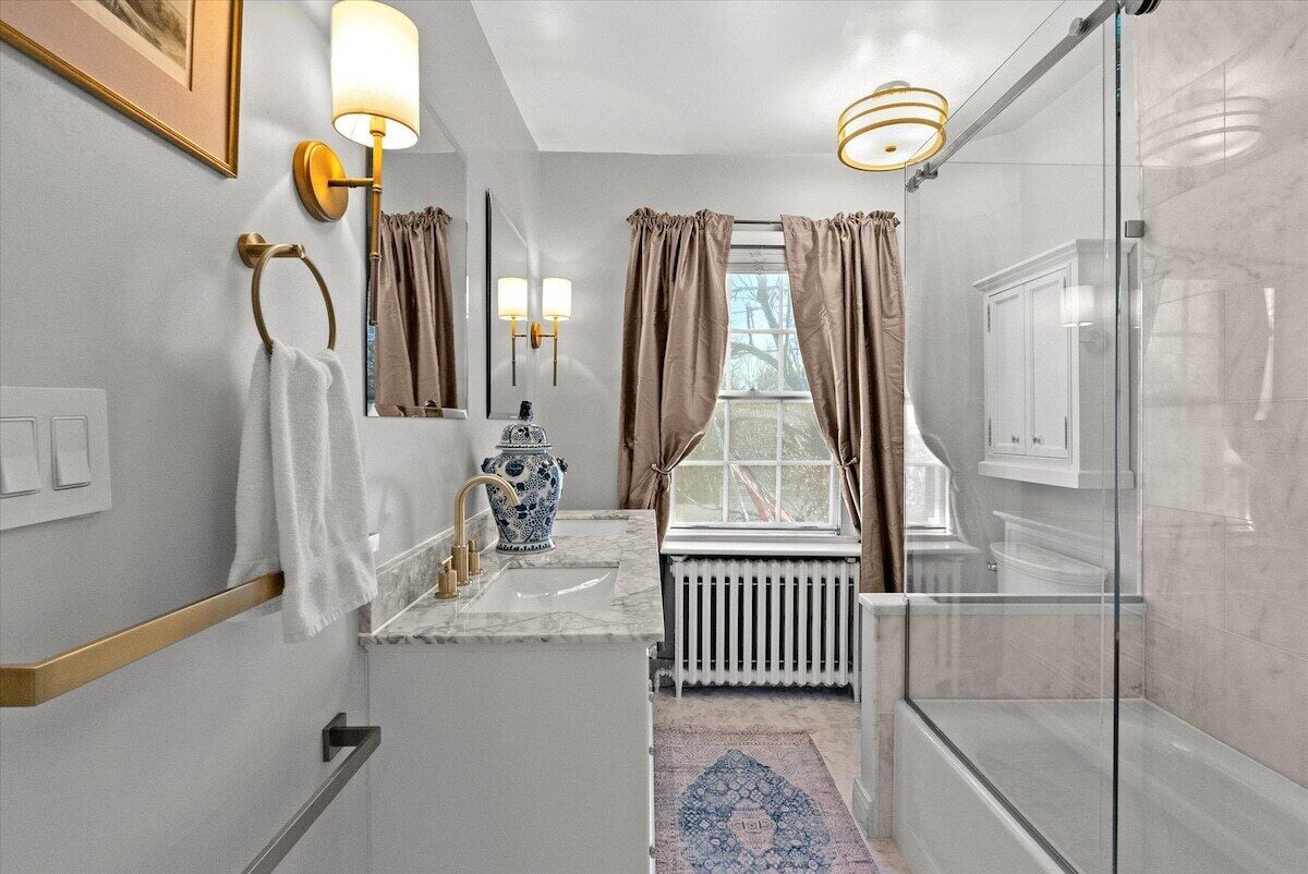 A modern bathroom with a marble sink, a vase, a radiator, and a glass shower enclosure.