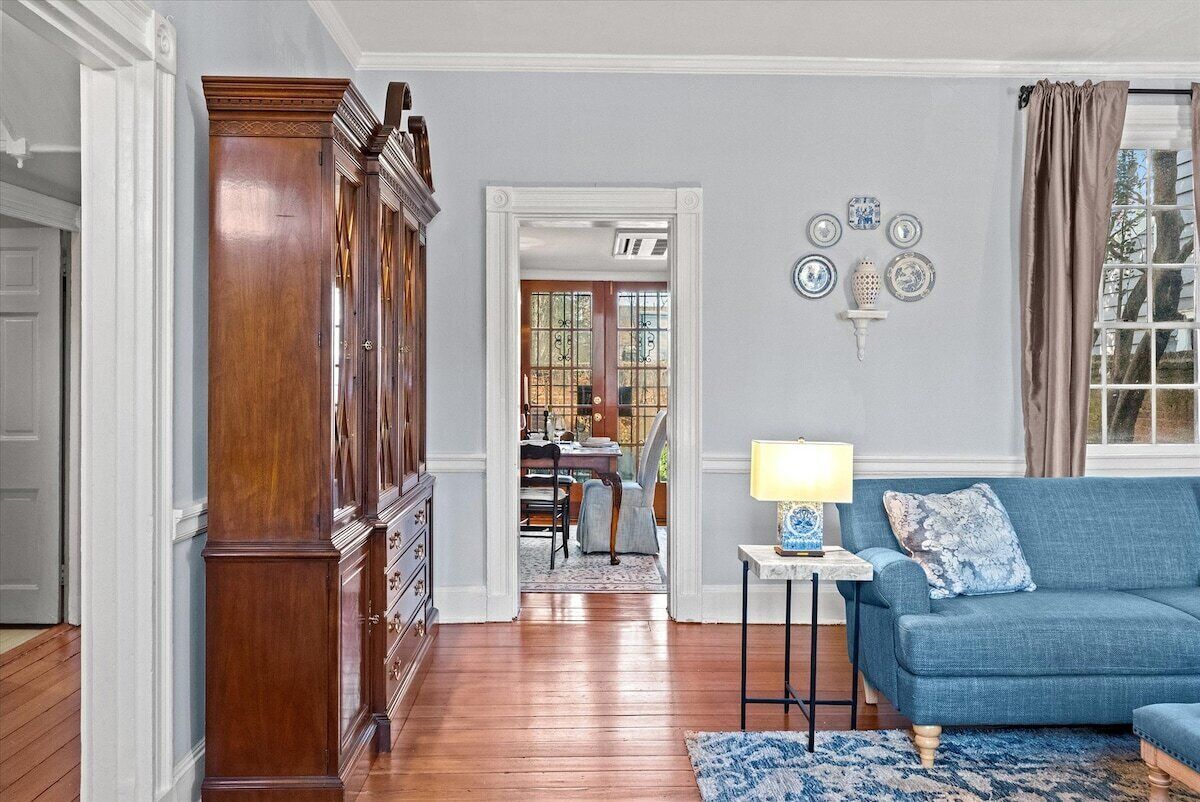 Una sala de estar con un sofá azul, un mueble de madera y un comedor al fondo.
