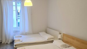 Een hotelkamer met twee eenpersoonsbedden, houten hoofdeinden, een hanglamp en een raam met gordijnen.