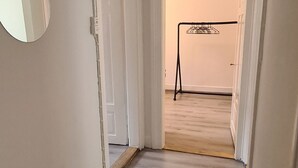 Een smalle gang met houten vloer, witte wanden en een deur naar een andere kamer.