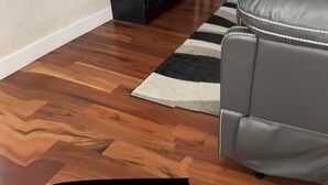 A modern living room with a flat-screen TV mounted on the wall, a dark entertainment unit, a grey leather sofa, a patterned rug, and a small side table with a lamp. - Cozy Stay near UCHealth and Anschutz Hospitals  (Aurora)