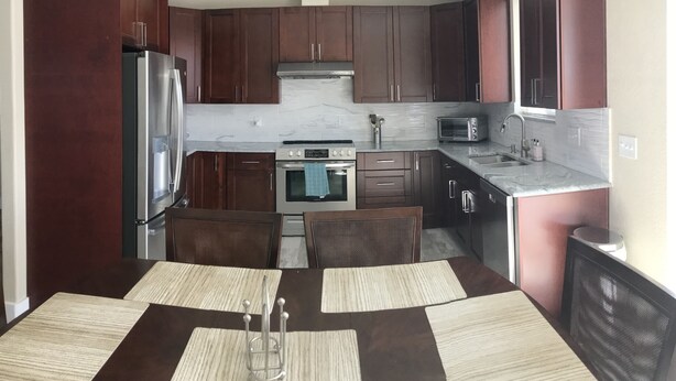 A modern kitchen with dark wooden cabinets, stainless steel appliances, and a marble backsplash. - Cozy Stay near UCHealth and Anschutz Hospitals  (Aurora)
