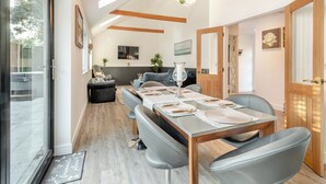 Ein moderner Essbereich mit einem langen Tisch, gedeckt für sechs Personen, Holzbalken an der Decke und einem großen Fenster, das natürliches Licht hereinlässt.