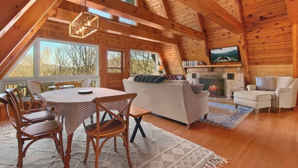 Amplia zona de estar tipo loft con chimenea, vigas de madera y ventanas grandes.
