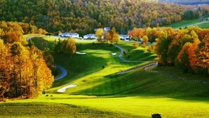 Un campo de golf con un sendero sinuoso, un estanque y casas al fondo.