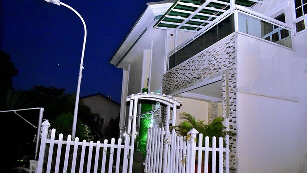 A gated entrance to a building with a white picket fence, a street lamp, and a small garden area with plants. - Viola Apartments & Suites (Abuja)