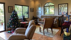 Ein gemütliches Wohnzimmer mit Weihnachtsbaum, bequemen Sitzgelegenheiten und großen Fenstern mit Blick ins Freie.