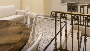 A modern living room with a round wooden table and white furniture, a staircase with ornate metal railings, and a kitchen with white cabinets and a built-in oven. - 2 bedroom apartment in venice (Venezia)