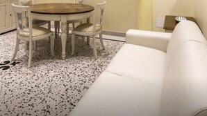 A dining area with a round table and four chairs, a white sofa, and a kitchen area with cabinets. - 2 bedroom apartment in venice (Venezia)