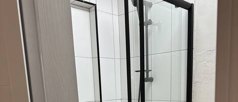 A glass-enclosed shower with a black frame, white tiled walls, and a wooden floor.