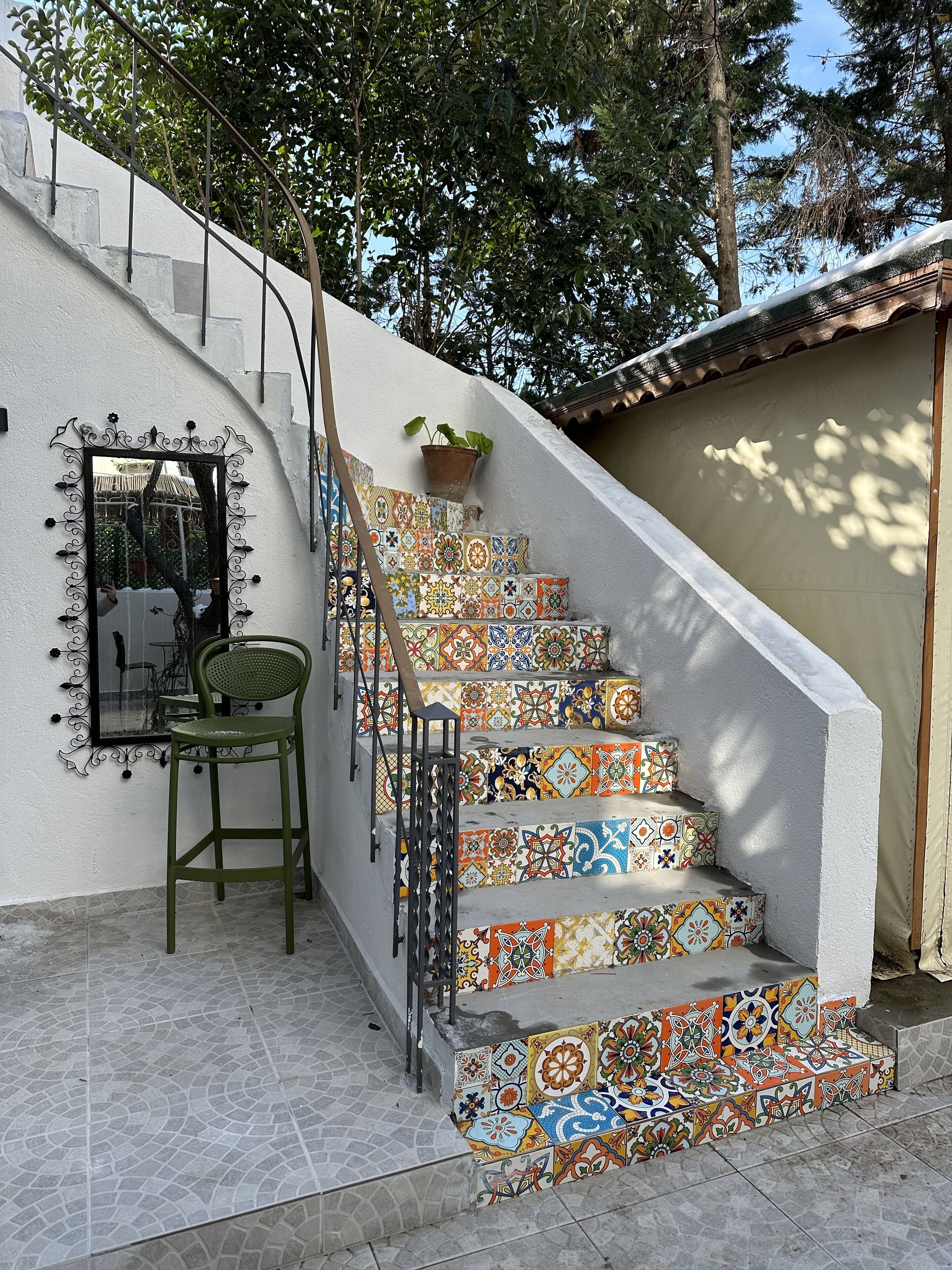 Una escalera con baldosas de colores, una silla verde y una planta en maceta.