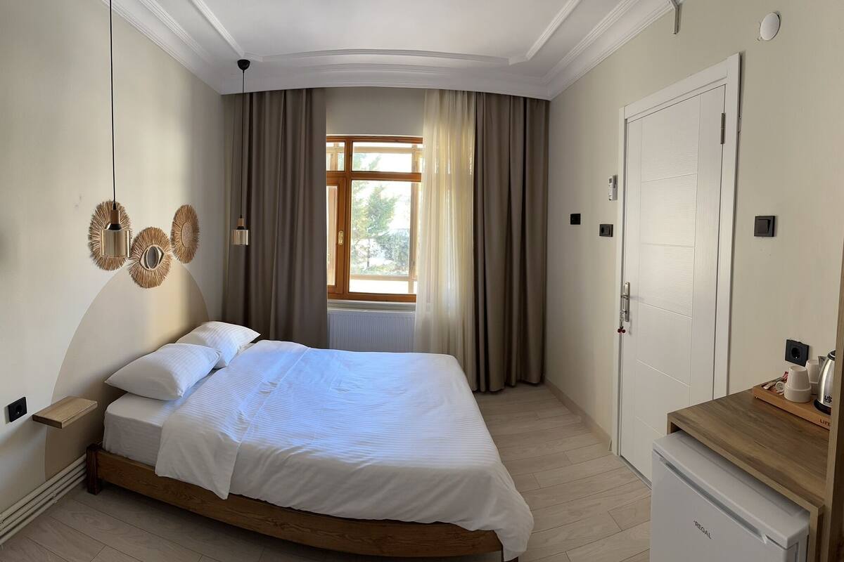 A bedroom with a bed, a nightstand, a wooden bedside table, a window with curtains, and a door.