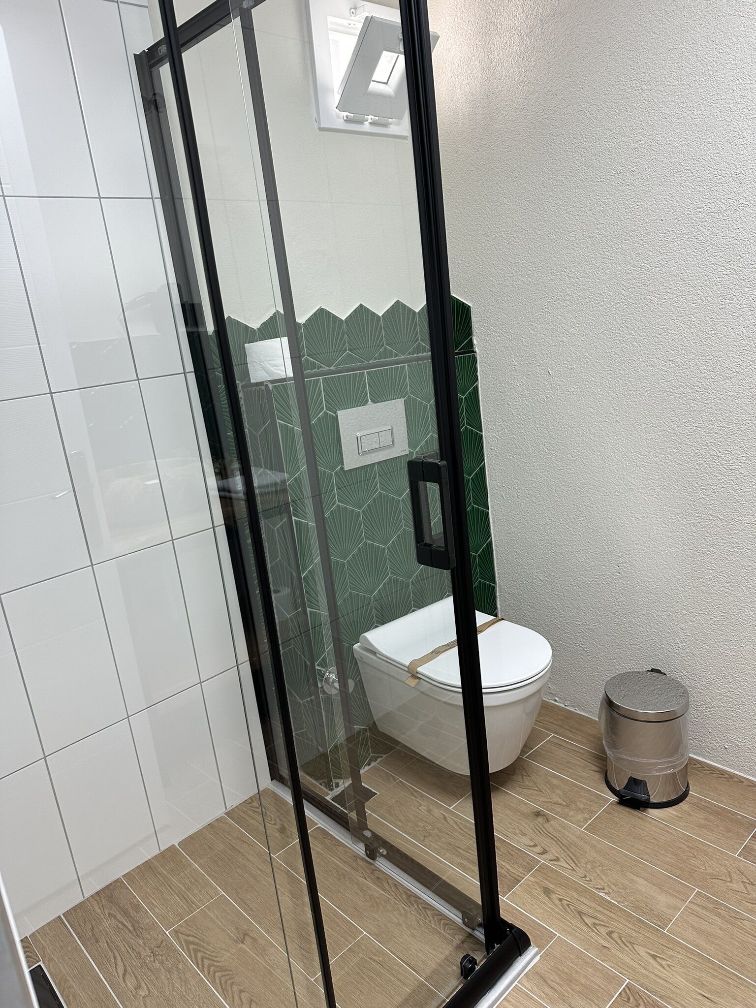 A modern bathroom with a glass shower enclosure, a toilet, and a trash bin.
