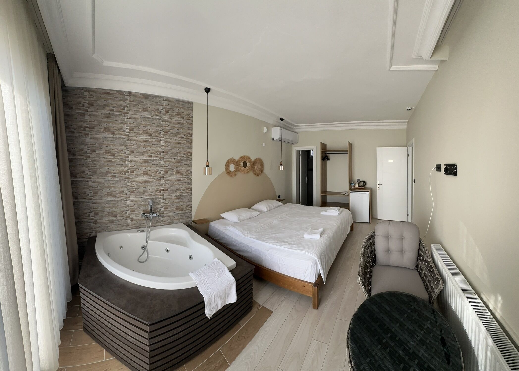 A modern bedroom with a large bed, a separate bathroom with a bathtub, a small desk, and a chair.