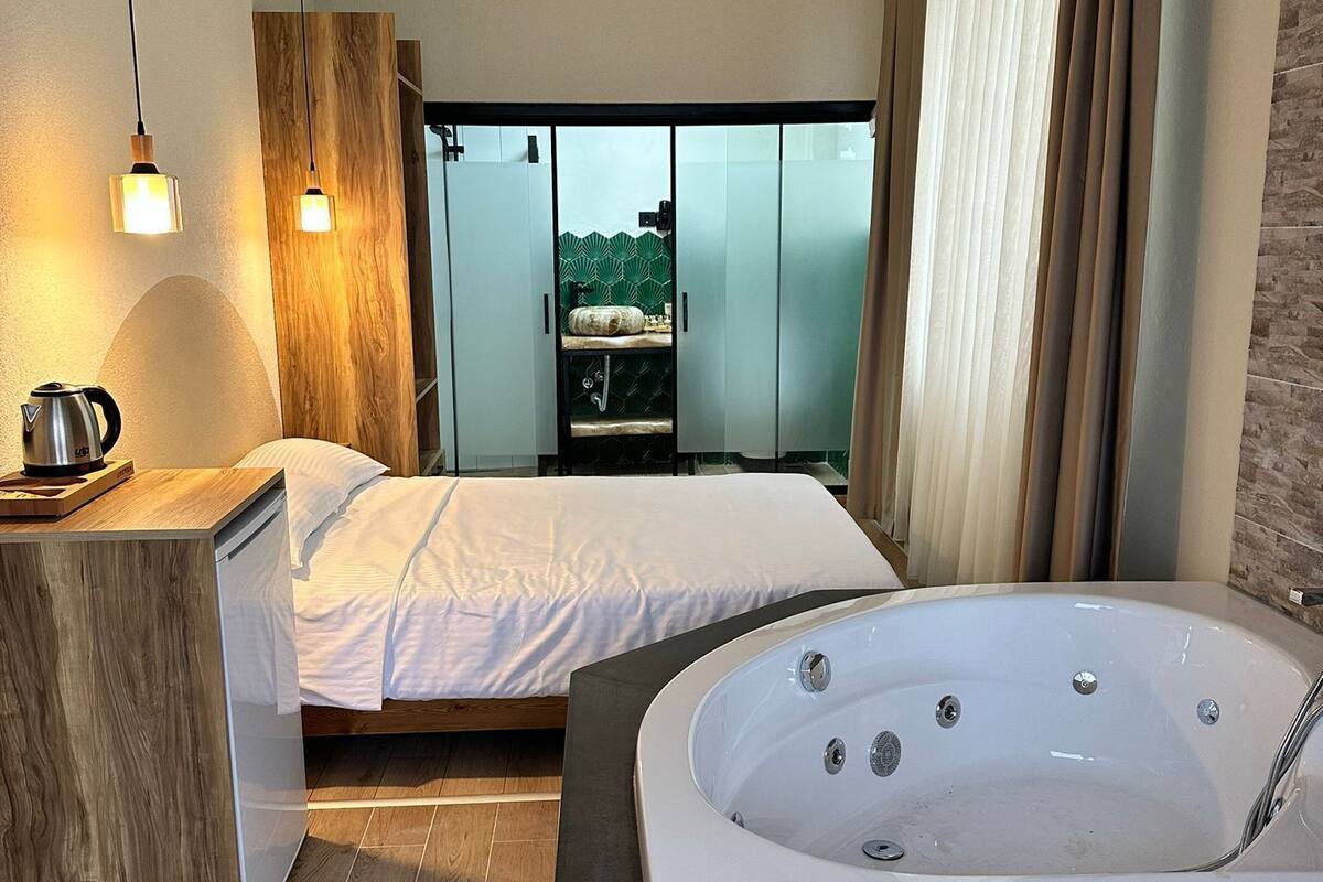 A modern bedroom with a large bed, a separate bathroom with a bathtub, and a view of a balcony.