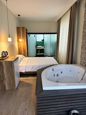 A modern bedroom with a large bed, a separate bathroom with a bathtub, and a view of a balcony. - Kingway Suite (Tekirdag)